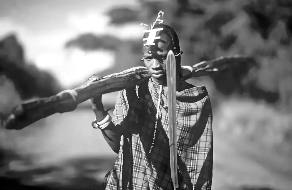 Ein junger Massai (Elmoran) mit einem Holzstab (Rungu) und einem Speer (Olamai)